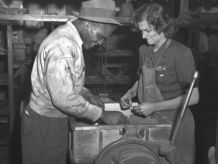 A black-and-white photo with a man and a woman working side-by-side in a factory.